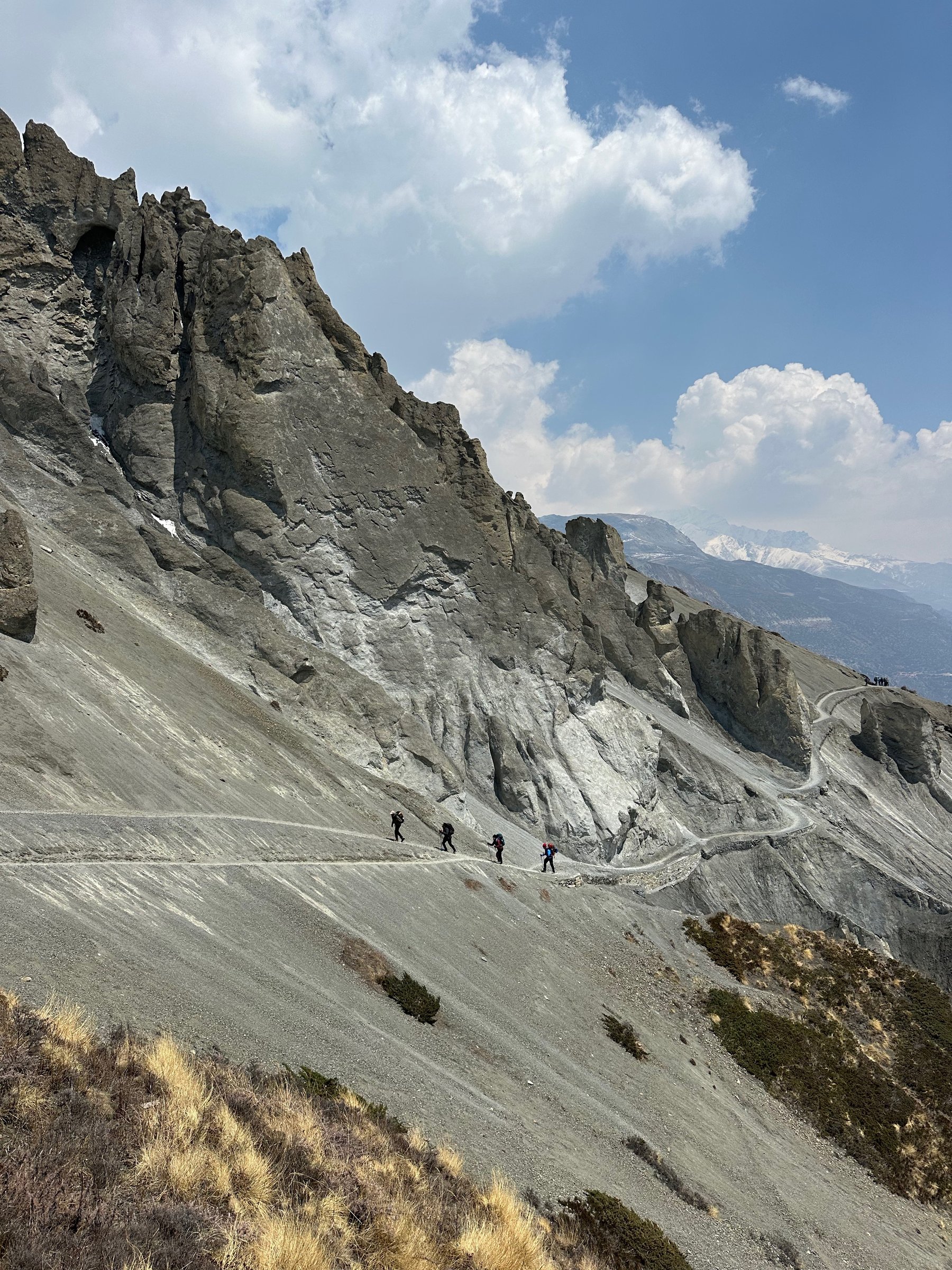 Hikers walking a mountain trail beneath dramatic peaks and clouds